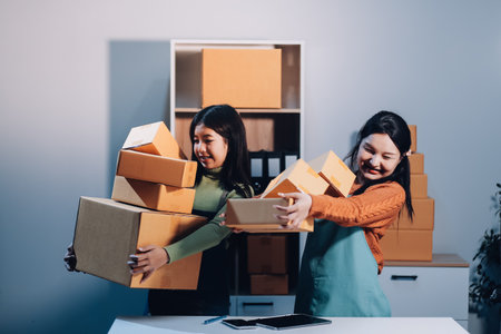 Startup SME small business entrepreneur of freelance Asian woman wearing apron using laptop and box to receive and review orders online to prepare to pack sell to customers, online sme business ideas.の写真素材