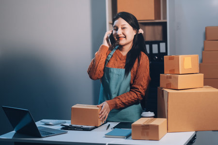 Startup SME small business entrepreneur of freelance Asian woman wearing apron using laptop and box to receive and review orders online to prepare to pack sell to customers, online sme business ideas.の写真素材