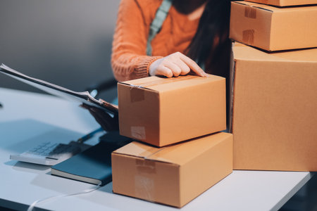 Startup SME small business entrepreneur of freelance Asian woman wearing apron using laptop and box to receive and review orders online to prepare to pack sell to customers, online sme business ideas.の写真素材