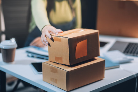 Startup SME small business entrepreneur of freelance Asian woman wearing apron using laptop and box to receive and review orders online to prepare to pack sell to customers, online sme business ideas.の写真素材