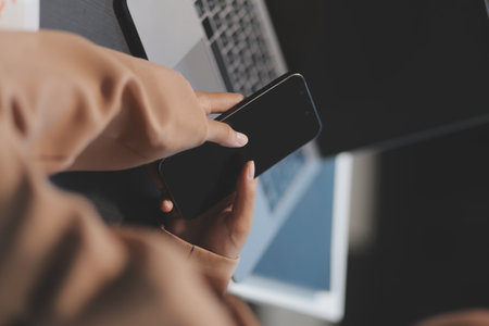 Young beautiful Asian businesswoman holding smartphone while working in the office room.の写真素材