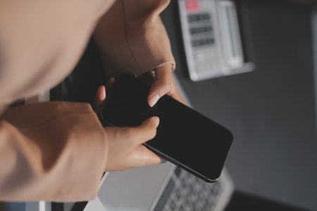 Young beautiful Asian businesswoman holding smartphone while working in the office room.の写真素材