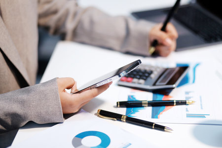Business woman using calculator and writing make note with calculate. Woman working at office with laptop and documents on his deskの写真素材