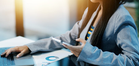 Asian businesswoman in formal suit in office happy and cheerful during using smartphone and workingの写真素材