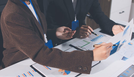 Focused young businessman signing agreement with skilled lawyer in eyeglasses. Concentrated financial advisor showing place for signature on paper contract document to male client at meeting in officeの写真素材