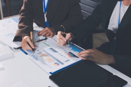 Focused young businessman signing agreement with skilled lawyer in eyeglasses. Concentrated financial advisor showing place for signature on paper contract document to male client at meeting in officeの写真素材