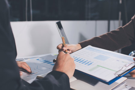Focused young businessman signing agreement with skilled lawyer in eyeglasses. Concentrated financial advisor showing place for signature on paper contract document to male client at meeting in officeの写真素材