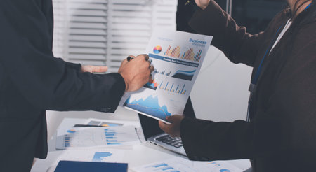 Focused young businessman signing agreement with skilled lawyer in eyeglasses. Concentrated financial advisor showing place for signature on paper contract document to male client at meeting in officeの写真素材