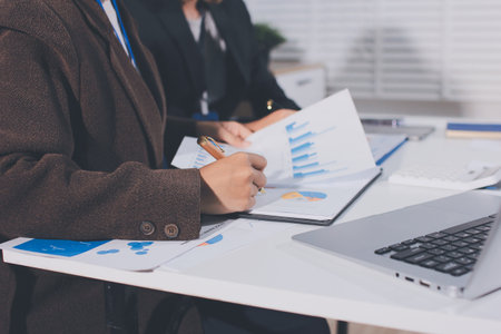 Focused young businessman signing agreement with skilled lawyer in eyeglasses. Concentrated financial advisor showing place for signature on paper contract document to male client at meeting in officeの写真素材