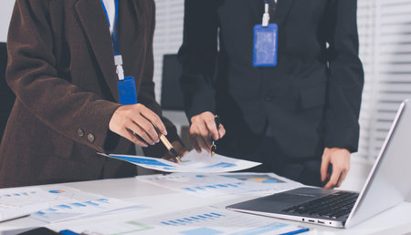 Focused young businessman signing agreement with skilled lawyer in eyeglasses. Concentrated financial advisor showing place for signature on paper contract document to male client at meeting in officeの写真素材