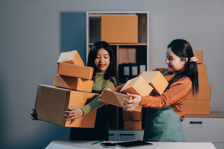 Startup SME small business entrepreneur of freelance Asian woman wearing apron using laptop and box to receive and review orders online to prepare to pack sell to customers, online sme business ideas.の写真素材