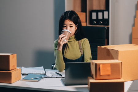 Startup SME small business entrepreneur of freelance Asian woman wearing apron using laptop and box to receive and review orders online to prepare to pack sell to customers, online sme business ideas.の写真素材