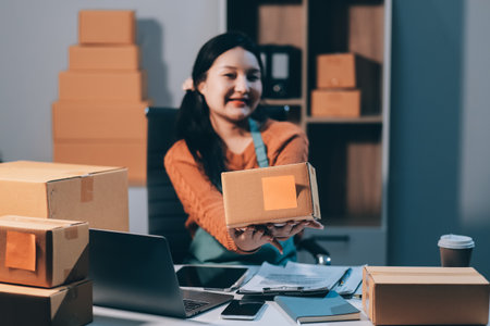 Startup SME small business entrepreneur of freelance Asian woman wearing apron using laptop and box to receive and review orders online to prepare to pack sell to customers, online sme business ideas.の写真素材