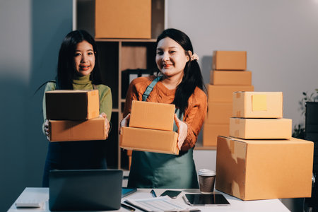 Startup SME small business entrepreneur of freelance Asian woman wearing apron using laptop and box to receive and review orders online to prepare to pack sell to customers, online sme business ideas.の写真素材