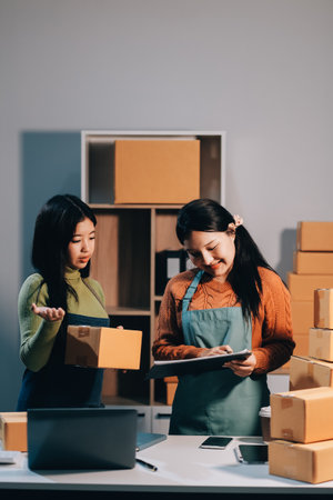 Startup SME small business entrepreneur of freelance Asian woman wearing apron using laptop and box to receive and review orders online to prepare to pack sell to customers, online sme business ideas.の写真素材