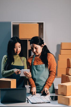 Startup SME small business entrepreneur of freelance Asian woman wearing apron using laptop and box to receive and review orders online to prepare to pack sell to customers, online sme business ideas.の写真素材