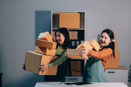 Startup SME small business entrepreneur of freelance Asian woman wearing apron using laptop and box to receive and review orders online to prepare to pack sell to customers, online sme business ideas.の写真素材