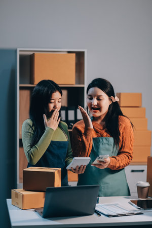 Startup SME small business entrepreneur of freelance Asian woman wearing apron using laptop and box to receive and review orders online to prepare to pack sell to customers, online sme business ideas.の写真素材