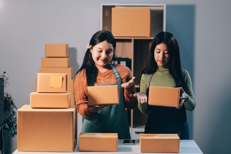 Startup SME small business entrepreneur of freelance Asian woman wearing apron using laptop and box to receive and review orders online to prepare to pack sell to customers, online sme business ideas.の写真素材