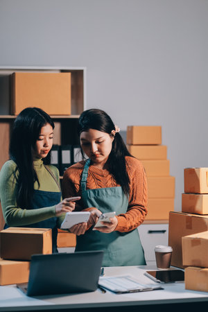 Startup SME small business entrepreneur of freelance Asian woman wearing apron using laptop and box to receive and review orders online to prepare to pack sell to customers, online sme business ideas.の写真素材