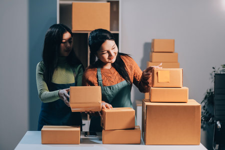 Startup SME small business entrepreneur of freelance Asian woman wearing apron using laptop and box to receive and review orders online to prepare to pack sell to customers, online sme business ideas.の写真素材