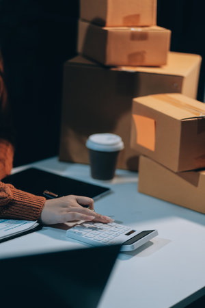 Startup SME small business entrepreneur of freelance Asian woman wearing apron using laptop and box to receive and review orders online to prepare to pack sell to customers, online sme business ideas.の写真素材