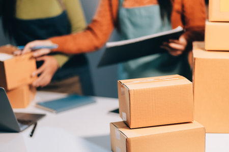 Startup SME small business entrepreneur of freelance Asian woman wearing apron using laptop and box to receive and review orders online to prepare to pack sell to customers, online sme business ideas.の写真素材