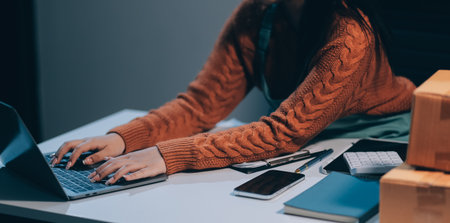 Startup SME small business entrepreneur of freelance Asian woman wearing apron using laptop and box to receive and review orders online to prepare to pack sell to customers, online sme business ideas.の写真素材