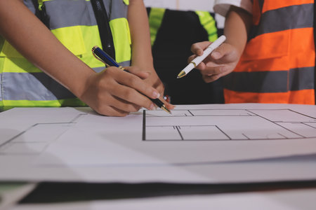 Closeup of team of industrial engineers meeting analyze machinery blueprints consult project on table in manufacturing factory. Working in manufacturing plant or production plant.の写真素材