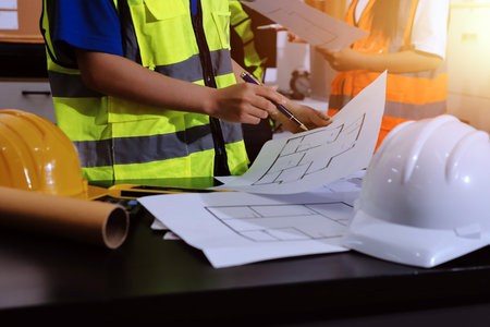 Closeup of team of industrial engineers meeting analyze machinery blueprints consult project on table in manufacturing factory. Working in manufacturing plant or production plant.の写真素材