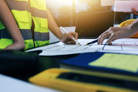Closeup of team of industrial engineers meeting analyze machinery blueprints consult project on table in manufacturing factory. Working in manufacturing plant or production plant.の写真素材