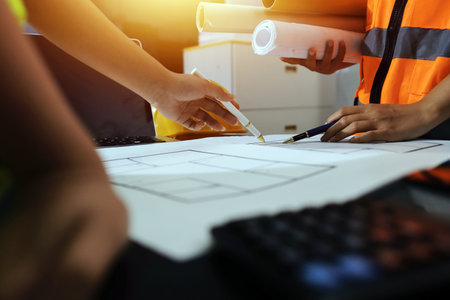 Closeup of team of industrial engineers meeting analyze machinery blueprints consult project on table in manufacturing factory. Working in manufacturing plant or production plant.の写真素材