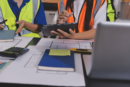 Closeup of team of industrial engineers meeting analyze machinery blueprints consult project on table in manufacturing factory. Working in manufacturing plant or production plant.の写真素材