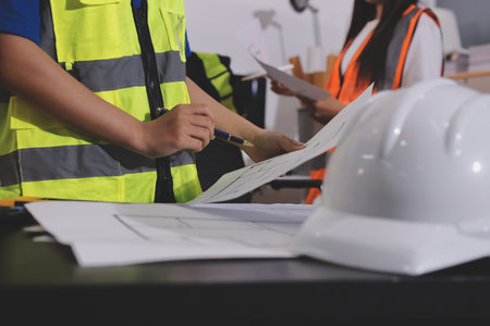 Closeup of team of industrial engineers meeting analyze machinery blueprints consult project on table in manufacturing factory. Working in manufacturing plant or production plant.の写真素材
