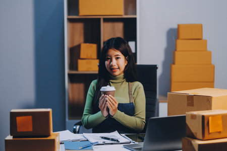 Startup SME small business entrepreneur of freelance Asian woman wearing apron using laptop and box to receive and review orders online to prepare to pack sell to customers, online sme business ideas.の写真素材