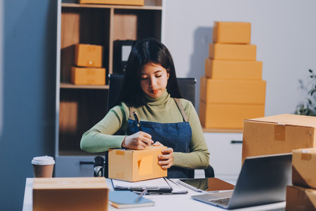 Startup SME small business entrepreneur of freelance Asian woman wearing apron using laptop and box...