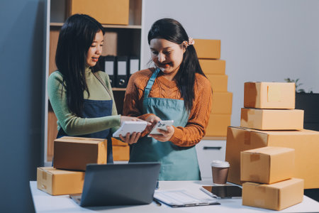 Startup SME small business entrepreneur of freelance Asian woman wearing apron using laptop and box to receive and review orders online to prepare to pack sell to customers, online sme business ideas.の写真素材