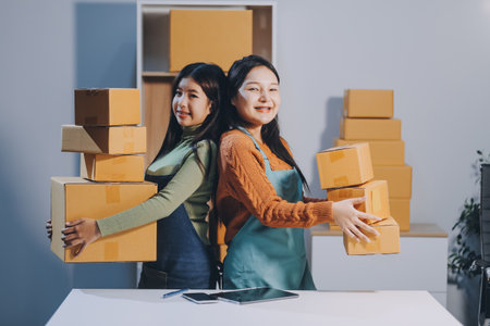 Startup SME small business entrepreneur of freelance Asian woman wearing apron using laptop and box to receive and review orders online to prepare to pack sell to customers, online sme business ideas.の写真素材
