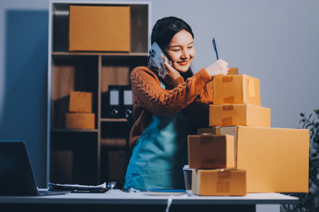 Startup SME small business entrepreneur of freelance Asian woman wearing apron using laptop and box to receive and review orders online to prepare to pack sell to customers, online sme business ideas.の写真素材