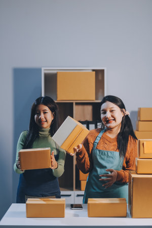 Startup SME small business entrepreneur of freelance Asian woman wearing apron using laptop and box to receive and review orders online to prepare to pack sell to customers, online sme business ideas.の写真素材