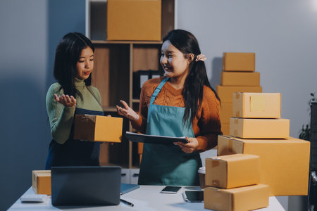 Startup SME small business entrepreneur of freelance Asian woman wearing apron using laptop and box to receive and review orders online to prepare to pack sell to customers, online sme business ideas.の写真素材