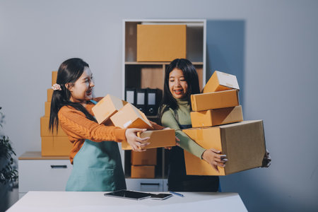 Startup SME small business entrepreneur of freelance Asian woman wearing apron using laptop and box to receive and review orders online to prepare to pack sell to customers, online sme business ideas.の写真素材