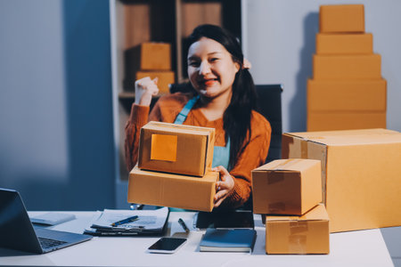 Startup SME small business entrepreneur of freelance Asian woman wearing apron using laptop and box to receive and review orders online to prepare to pack sell to customers, online sme business ideas.の写真素材