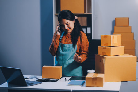 Startup SME small business entrepreneur of freelance Asian woman wearing apron using laptop and box to receive and review orders online to prepare to pack sell to customers, online sme business ideas.の写真素材