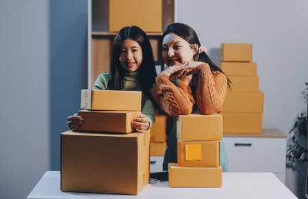 Startup SME small business entrepreneur of freelance Asian woman wearing apron using laptop and box to receive and review orders online to prepare to pack sell to customers, online sme business ideas.の写真素材