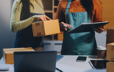 Startup SME small business entrepreneur of freelance Asian woman wearing apron using laptop and box to receive and review orders online to prepare to pack sell to customers, online sme business ideas.の写真素材