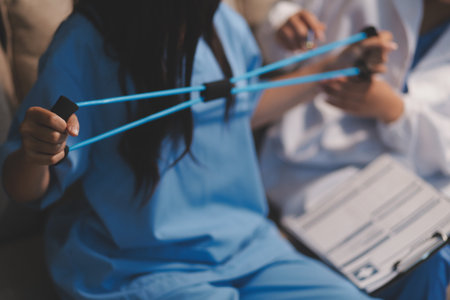 Doctor physiotherapist assisting a male patient while giving exercising treatment on stretching his arm with exercise band in the clinic, Rehabilitation physiotherapy conceptの写真素材