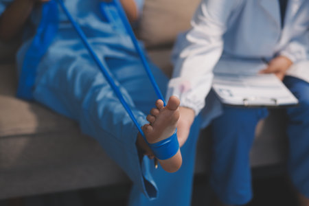 Confident physical therapist helps patient use resistance band stretching out his leg in clinic room.の写真素材
