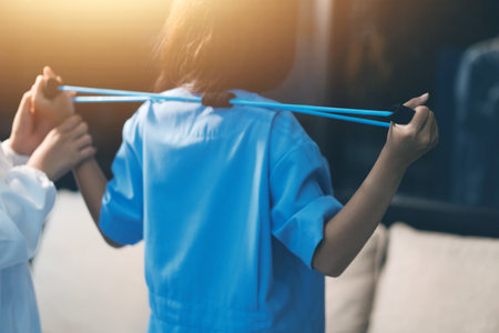Doctor physiotherapist assisting a male patient while giving exercising treatment on stretching his arm with exercise band in the clinic, Rehabilitation physiotherapy conceptの写真素材