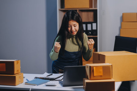 Startup SME small business entrepreneur of freelance Asian woman wearing apron using laptop and box to receive and review orders online to prepare to pack sell to customers, online sme business ideas.の写真素材